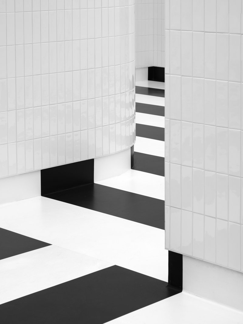 White tiled curved wall opening onto black and white striped floor pattern