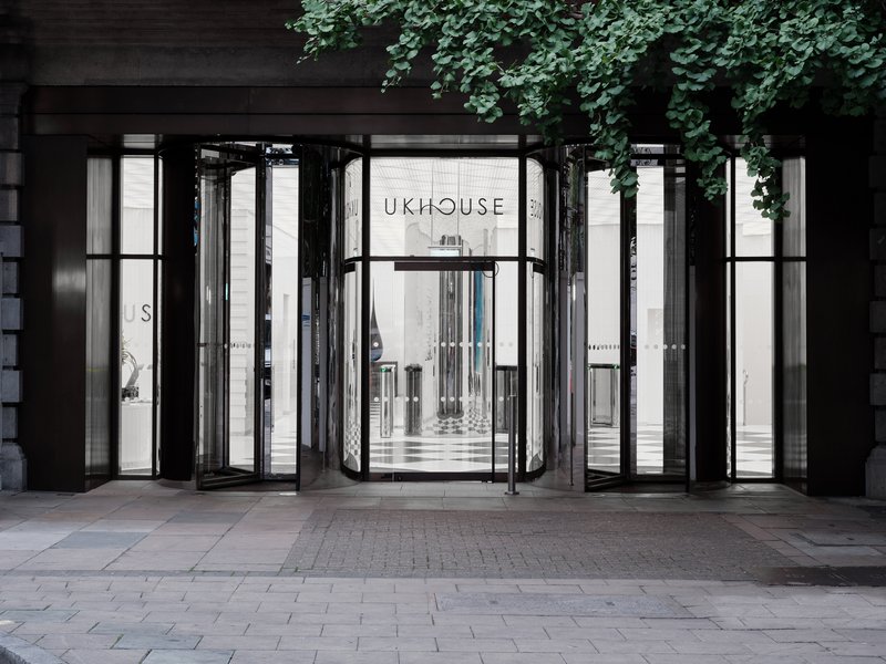 Street view of the glass folding door entrance framed by dark metal and overhanging ivy