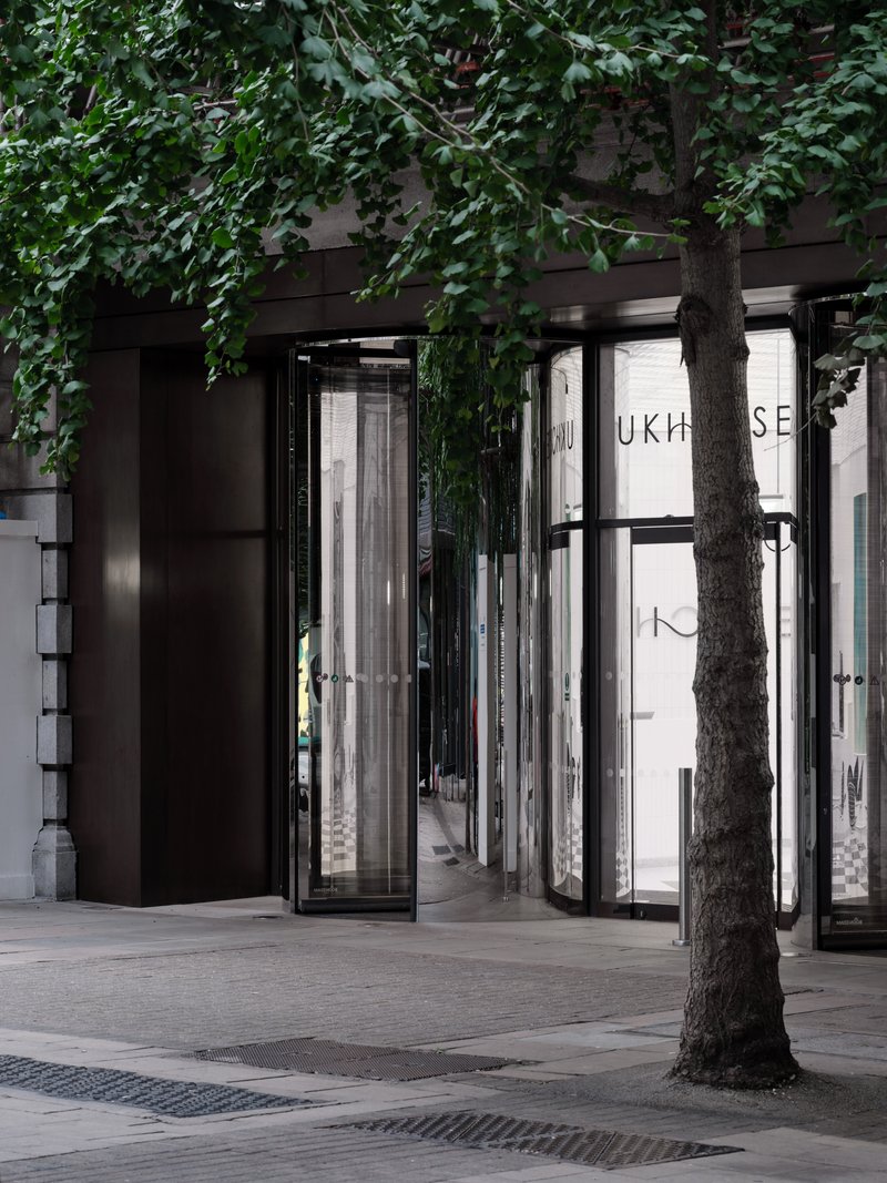 Street entrance with black framed glass doors and a tree trunk beneath overhanging ivy