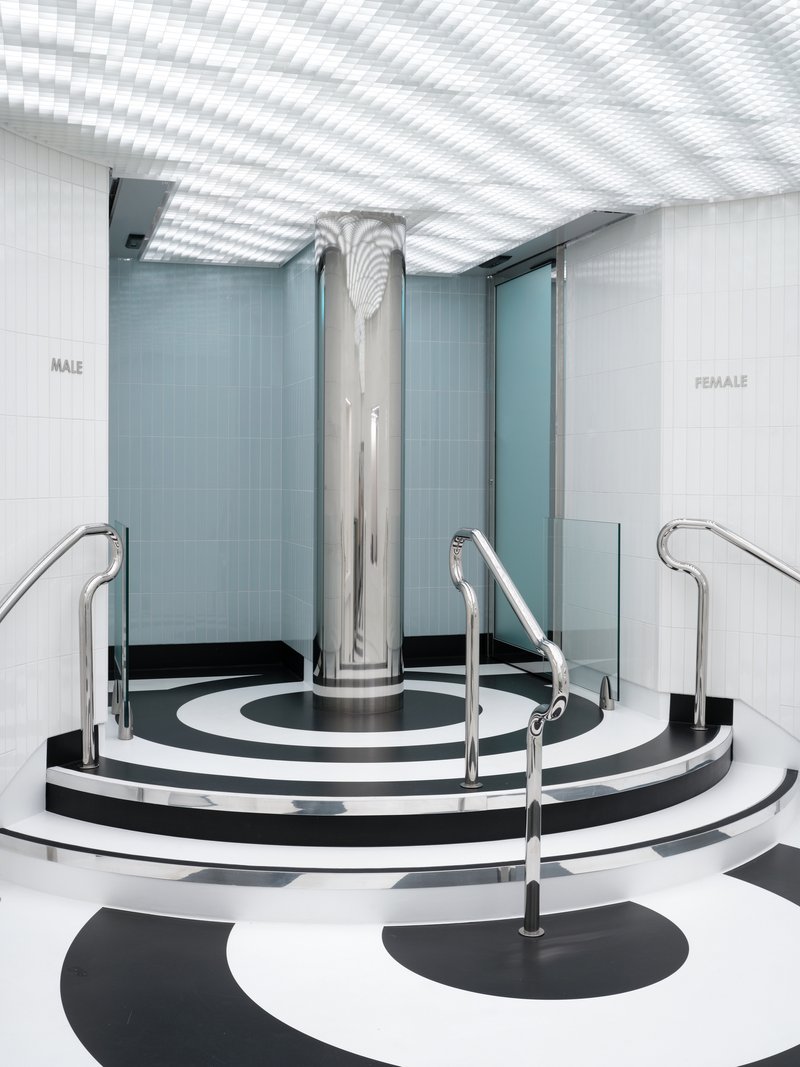 Circular platform with chrome column and handrails on concentric black and white striped flooring