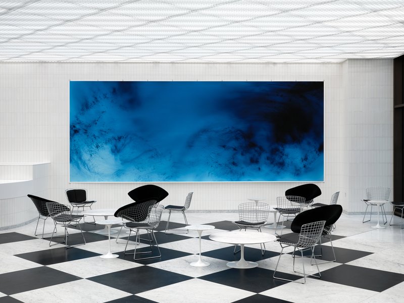 Seating area with wire mesh chairs beneath a large blue artwork on white tiled wall