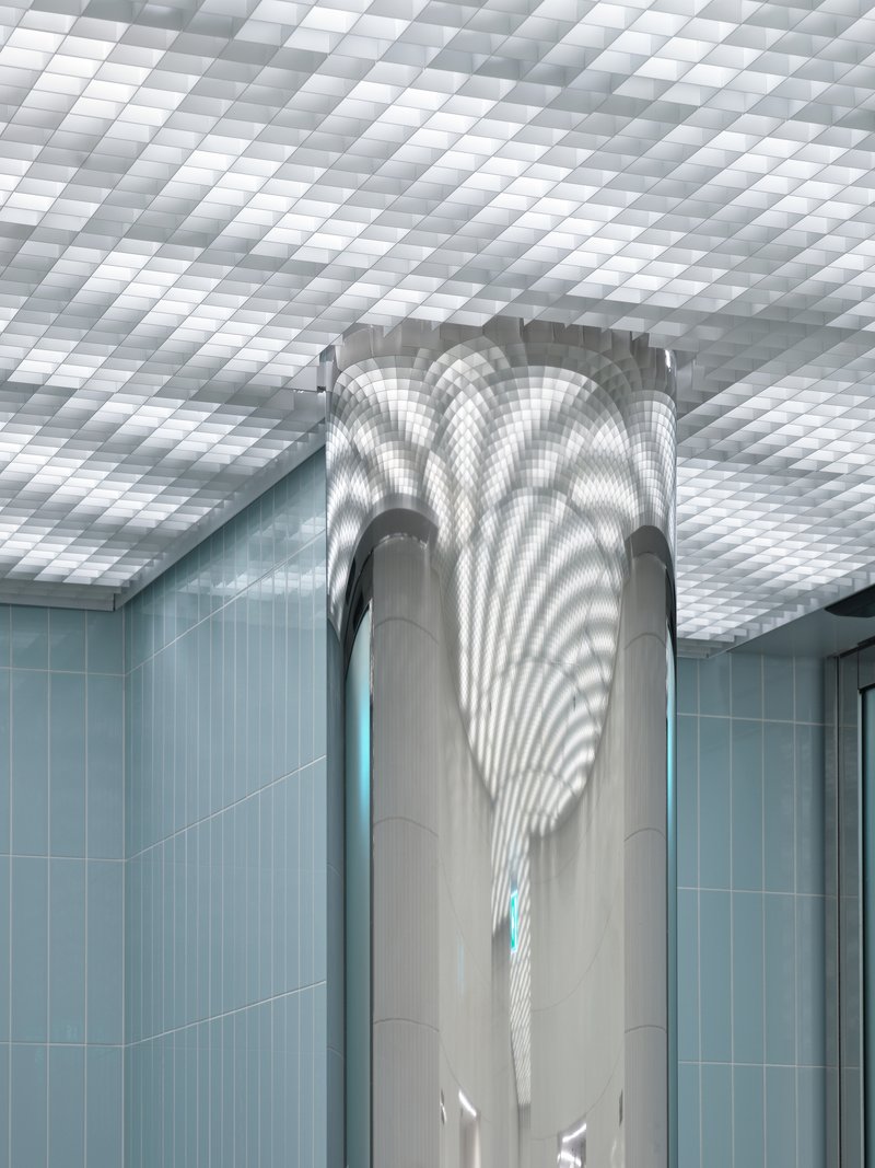 Central column wrapped in smooth paneling beneath a coffered translucent ceiling with light blue tiled walls