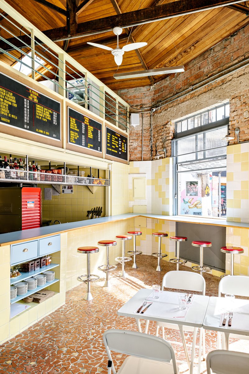 Dining space with timber ceiling, yellow tile walls, red bar stools and digital menu boards above the counter