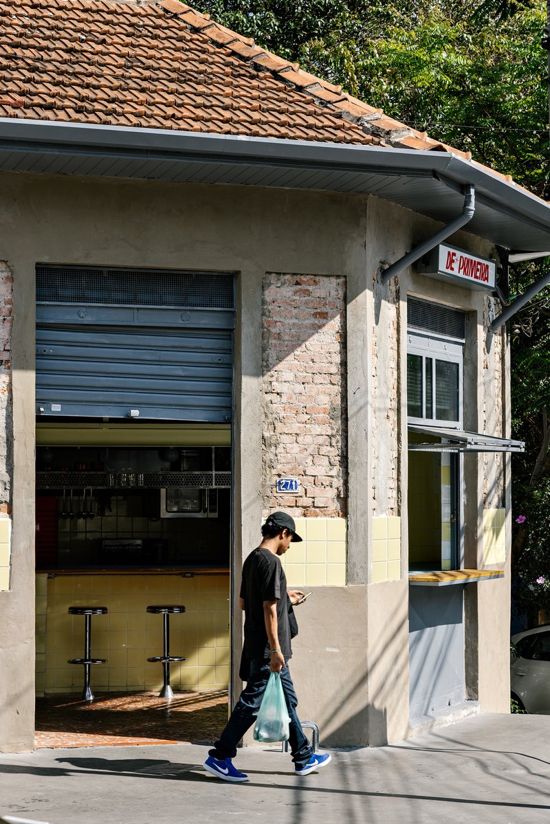 Corner facade with exposed brick patches and rolled shutter door with a pedestrian walking past in daylight