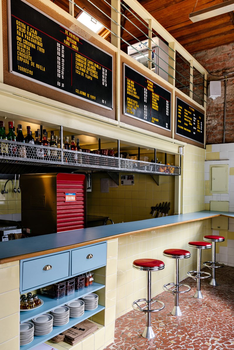 View of the bar counter showing exposed timber ceiling, digital menu screens and shelving with bottles