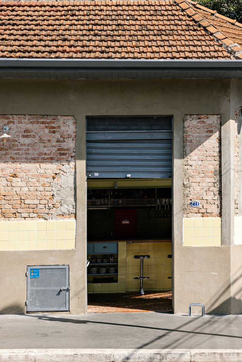 Street view of the facade showing terracotta tile roof, rolled shutter and patched plaster walls in sunlight