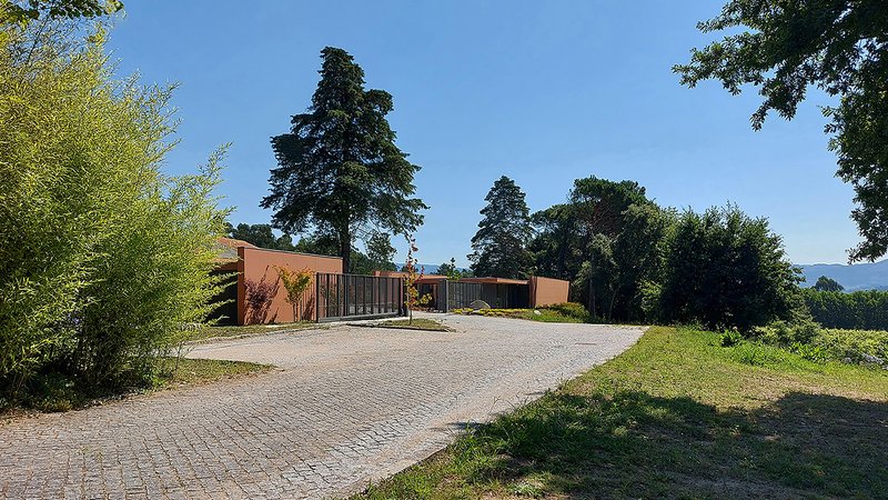 Cobblestone driveway curving toward the low-slung facade with perforated metal screen and tall conifer trees behind