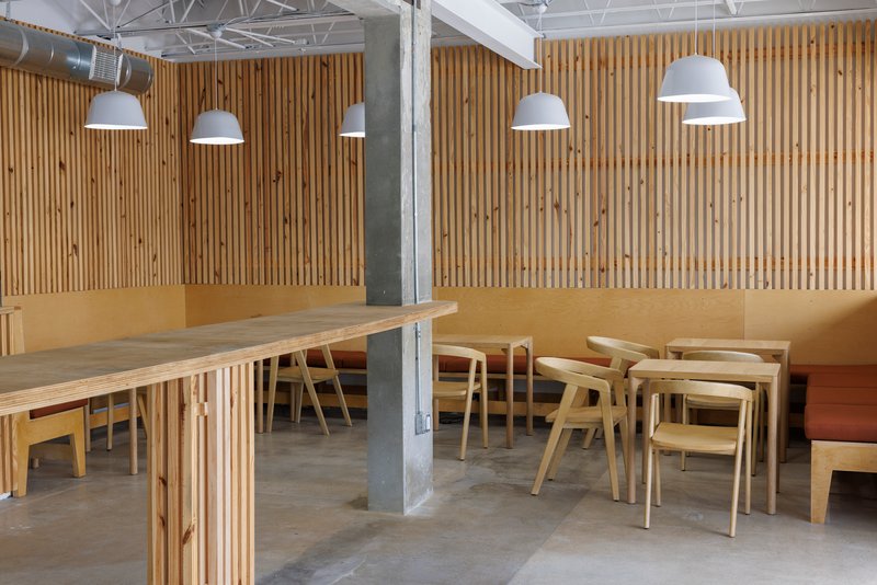 Seating zone with timber tables and chairs arranged around a raw concrete column