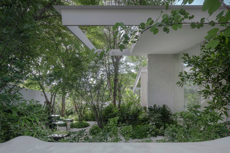 White concrete canopy and columns framing a planted courtyard with mature trees and dense foliage