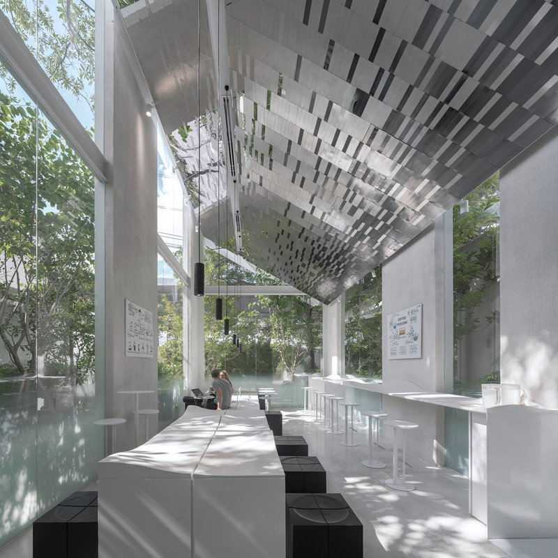 Interior seating area with white tables and black stools under geometric monochrome ceiling panels