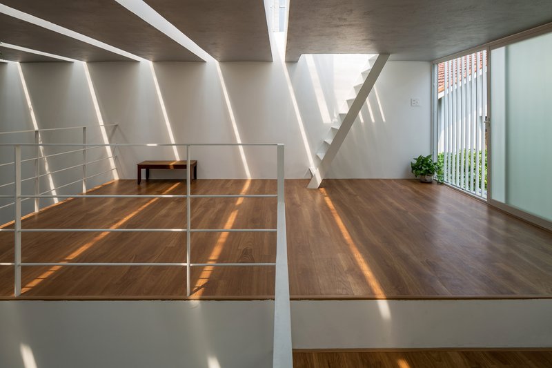Wood-floored mezzanine with white metal railing and diagonal light stripes from overhead skylights