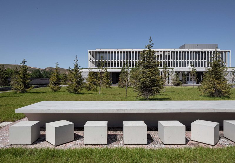 Outdoor seating area with concrete table and cube stools on a lawn before the vertical-louvered facade