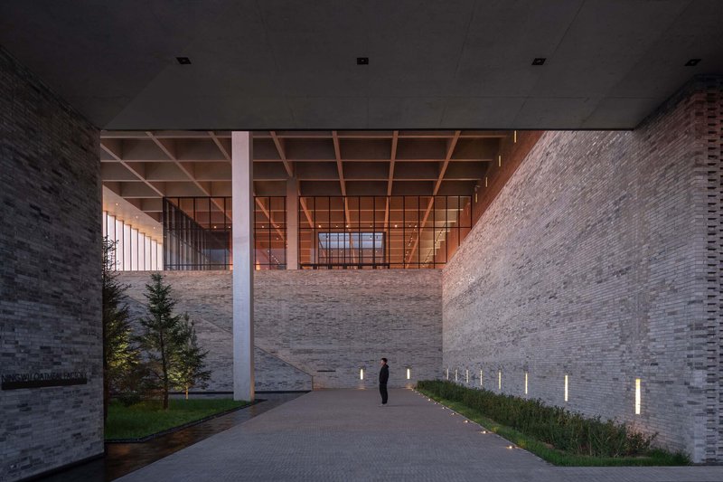 Covered entrance passage with timber coffered ceiling and a figure walking between masonry walls at twilight