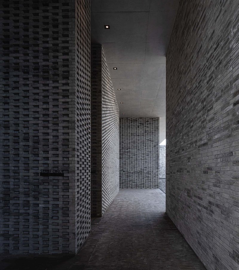 Narrow corridor with basketweave brick walls and recessed ceiling lights leading deeper into the space
