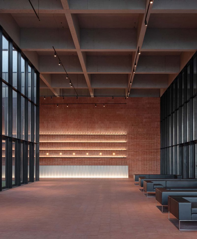 Timber coffered ceiling above a lobby with illuminated perforated brick wall and steel frame glazing
