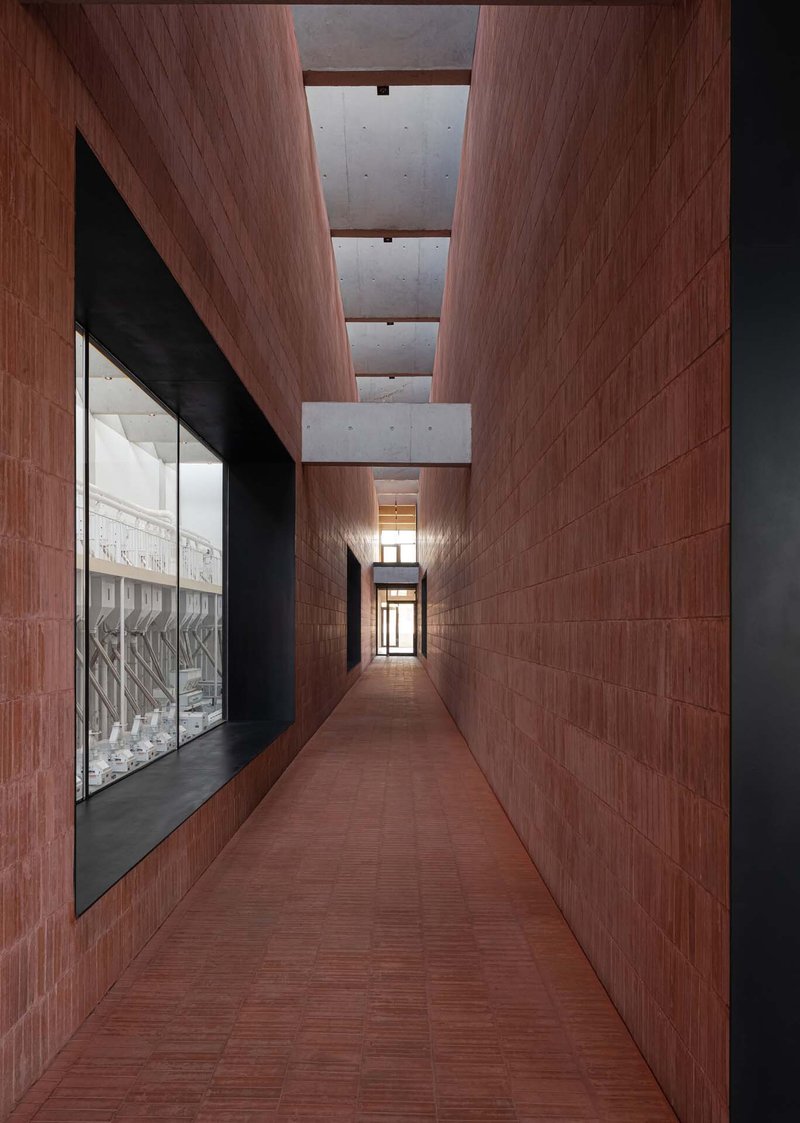 Narrow hallway clad in reddish timber panels with concrete ceiling beams and glazed display case