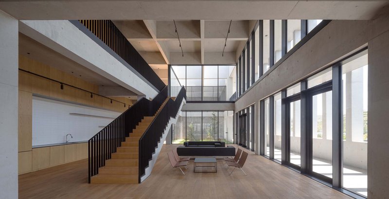 Double-height lobby with timber staircase, concrete coffered ceiling and floor-to-ceiling glazing overlooking trees
