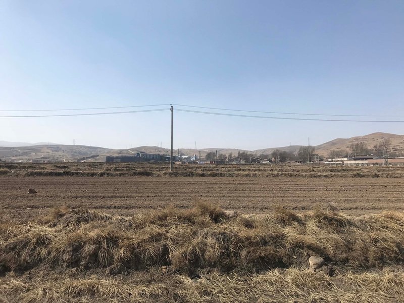 Distant view of the low-slung facility across bare agricultural fields under a winter sky
