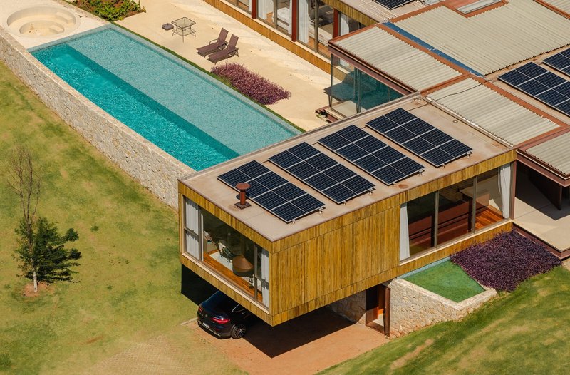 Aerial view of timber-clad volume with solar panels on the roof and lap pool on stone terrace