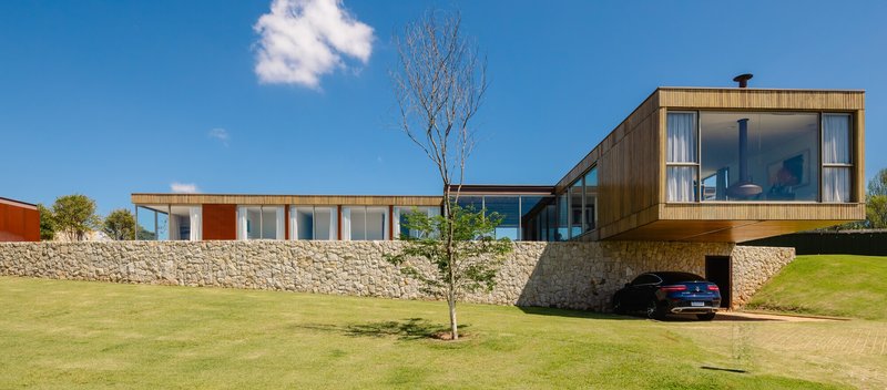 Horizontal facade with timber cladding and glass openings rising above a stone retaining wall
