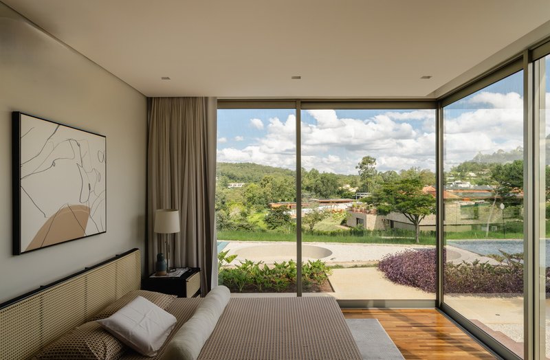 Bedroom with floor-to-ceiling glass doors opening to a garden with purple foliage and cloud-filled sky