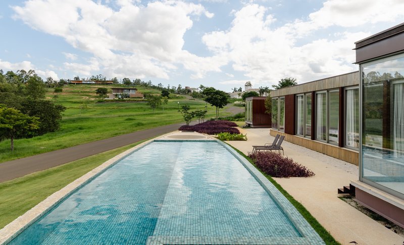 Long rectangular swimming pool with mosaic tile extending from the timber-clad volume toward a sloping green landscape