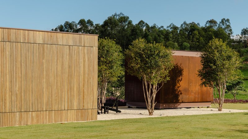 Horizontal timber cladding and weathered steel wall framing a recessed entrance with young trees in gravel