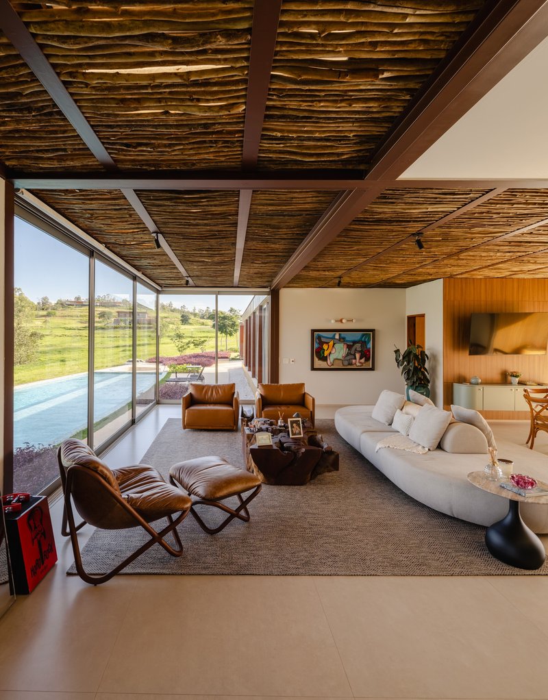 Living room with exposed timber-strip ceiling, floor-to-ceiling glazing and view to rolling landscape beyond pool terrace