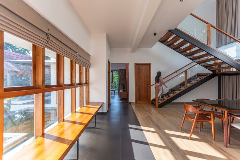 Interior hallway with open-tread timber staircase and continuous wood-framed glazing casting afternoon sunlight