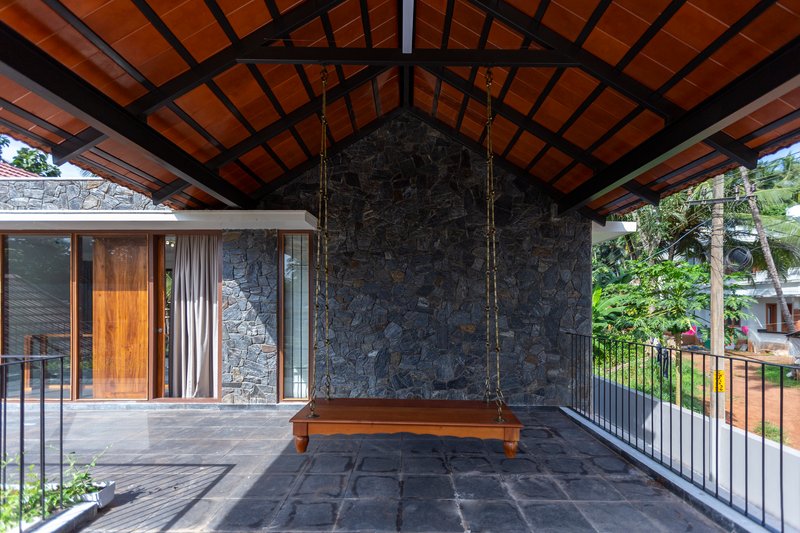 Covered terrace with exposed timber roof structure, dark stone wall and a suspended wooden swing