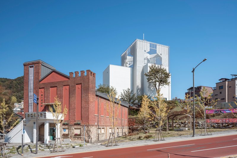 Street view of a white tower with decorative cornice rising beside a brick industrial building under clear skies