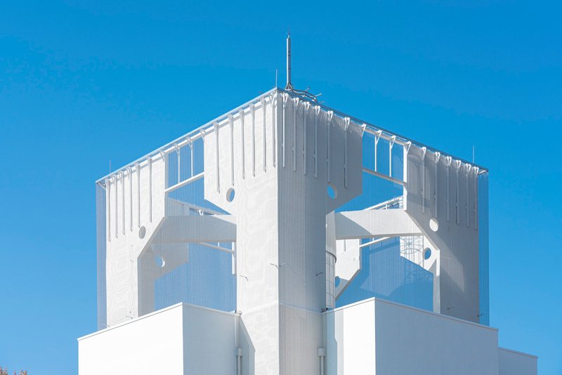 Close-up of the white corrugated tower crown with circular and geometric perforations and a central antenna