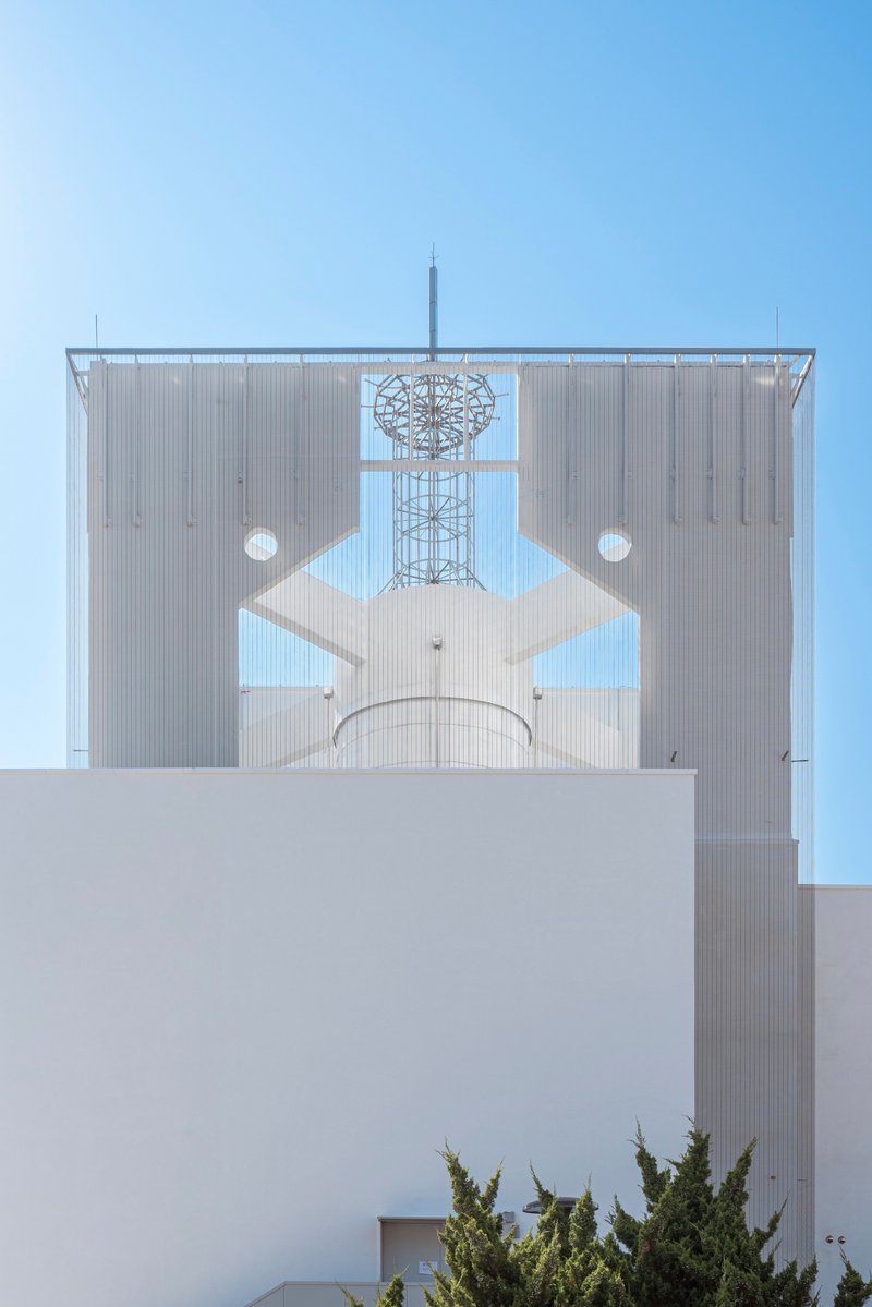 Metal screen facade with geometric cutouts framing a communications tower against clear blue sky