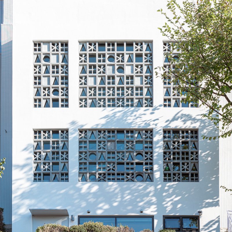 White stucco facade with geometric patterned window screens casting dappled tree shadows in daylight