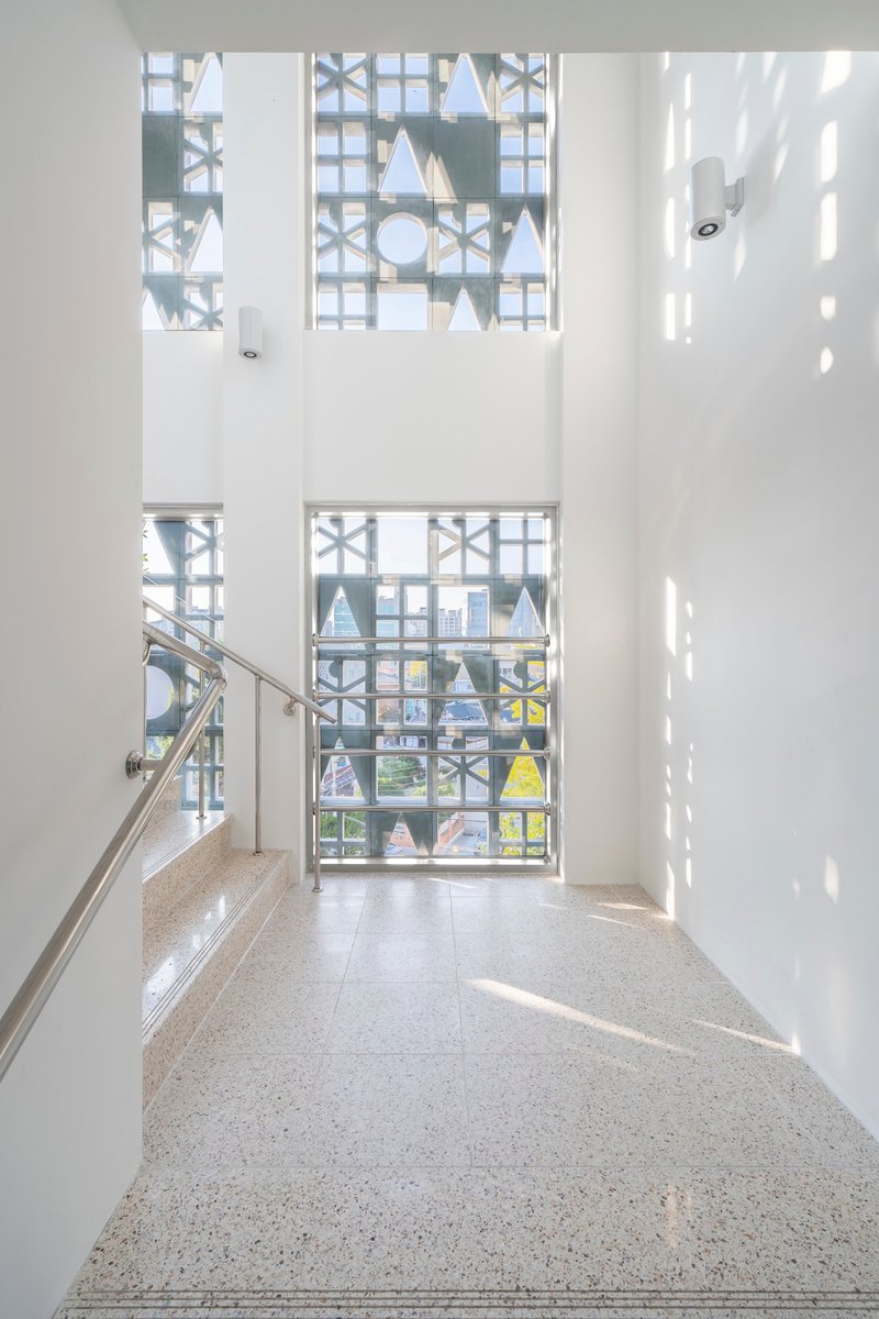Double-height stairwell with terrazzo flooring and geometric window screens filtering bright daylight patterns
