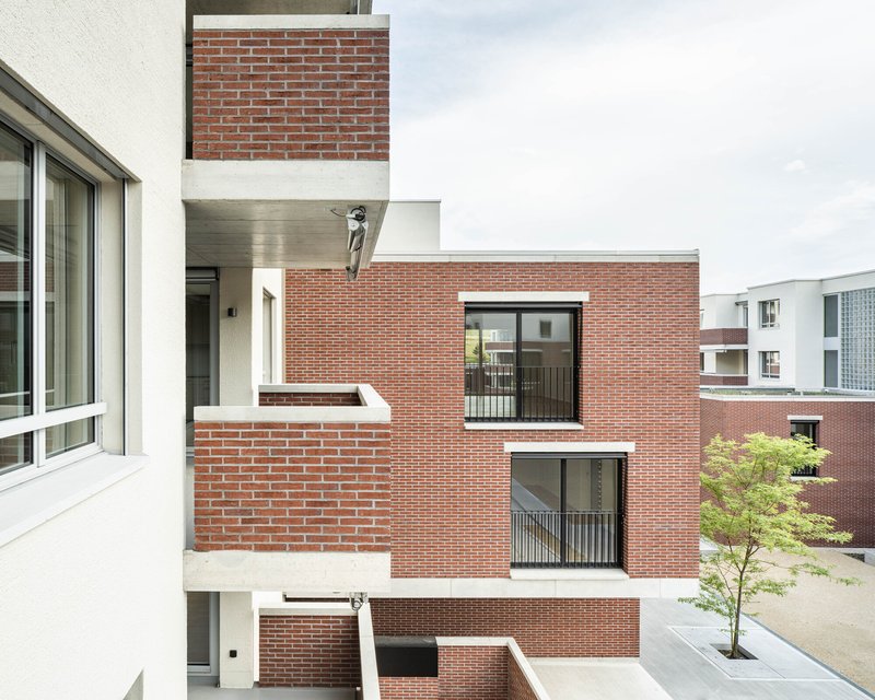Stacked brick balconies with metal railings and offset volumes facing courtyard with planted tree below
