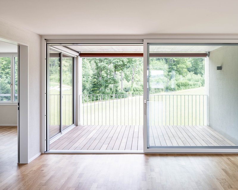 Interior room opening to timber deck balcony with vertical slat railing overlooking green landscape
