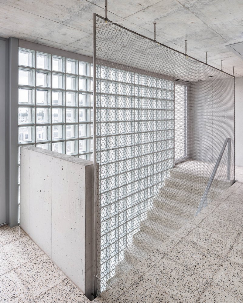 Interior corridor with patterned glass block partition and concrete balustrade beneath an exposed concrete ceiling