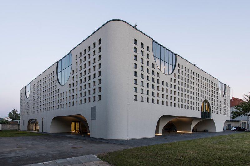 Long facade with repeating square window pattern and curved roofline under overcast evening sky