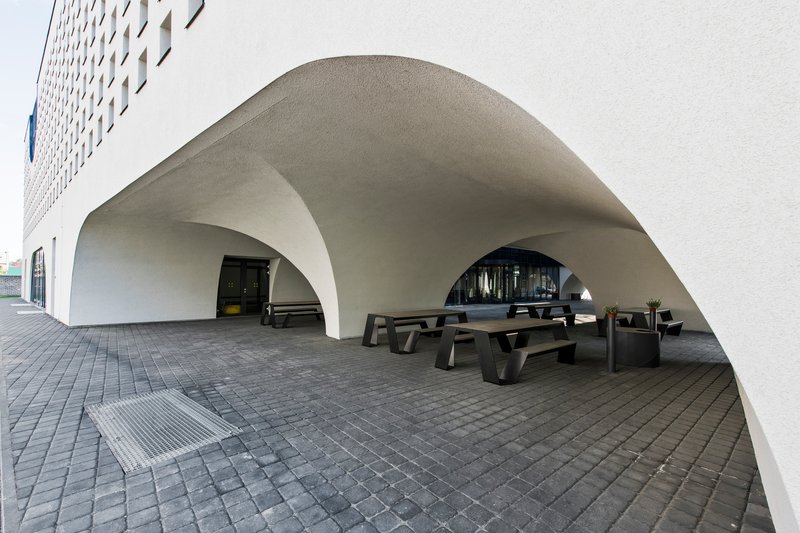 Covered terrace beneath vaulted white arches with dark timber benches on grey pavers