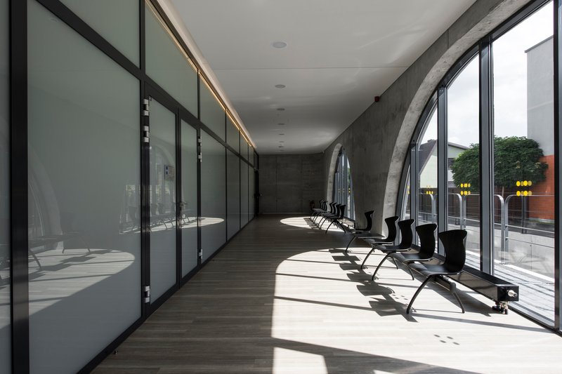 Glazed corridor with black metal frames along concrete wall and afternoon light on timber flooring