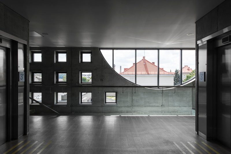 Interior lobby with curved window wall framing red tile roofs and square openings in dark concrete