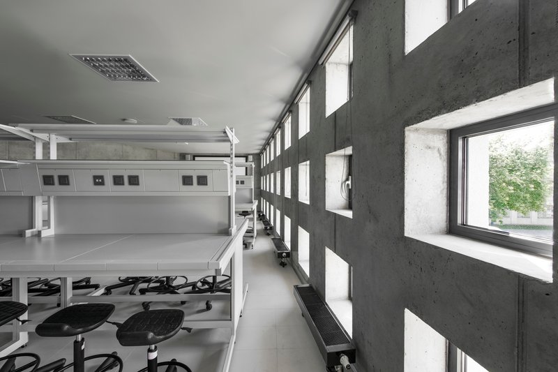Corridor with perforated concrete block wall filtering daylight beside open workroom