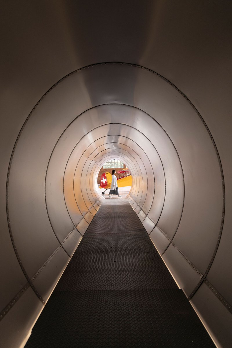 Curved tunnel corridor with ribbed metal walls and integrated strip lighting leading to the hangar floor