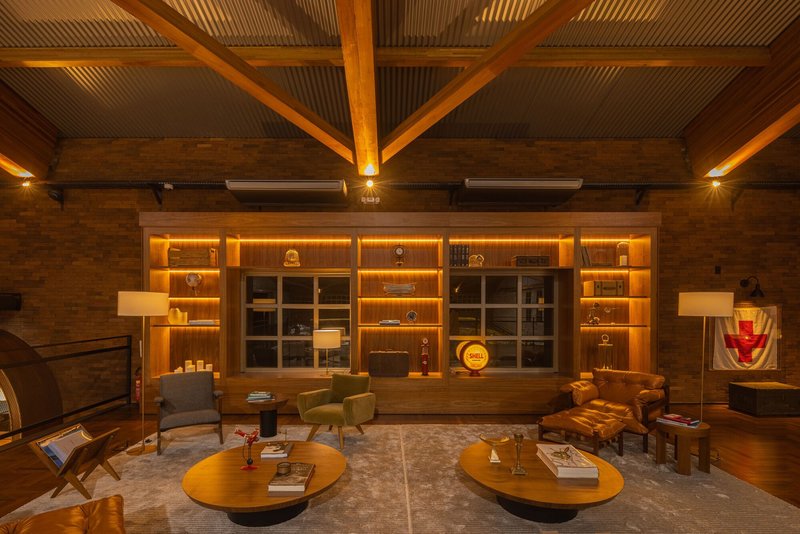 Evening view of the lounge space with backlit timber shelving and exposed brick walls under a vaulted roof