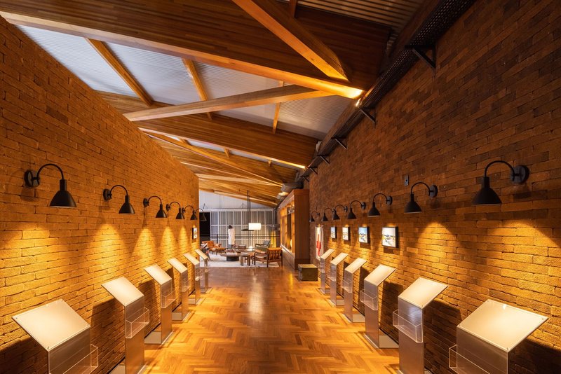 Gallery corridor with gooseneck wall sconces illuminating brick walls and herringbone timber flooring