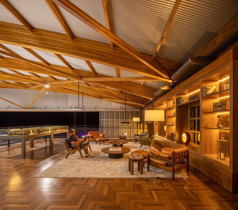 Open lounge area beneath sawtooth skylights with herringbone flooring and visitors seated near the display shelving