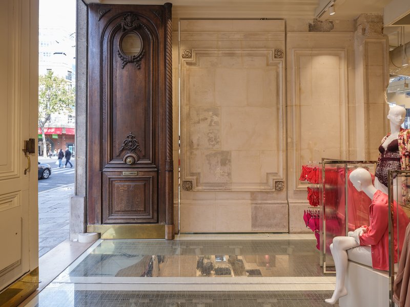 Ornate timber door propped open with stone paneled walls and glass floor revealing lower level