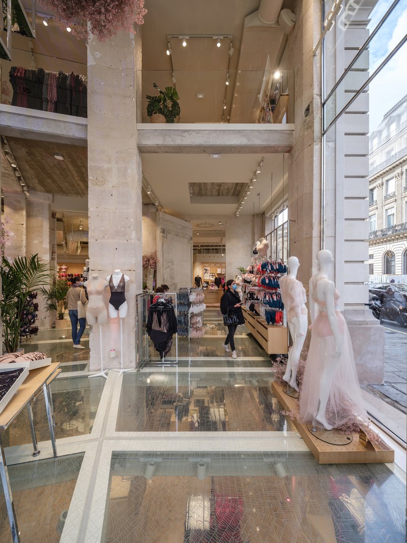 Multi-level retail space with glass floor panels and concrete columns framed by floor-to-ceiling street windows