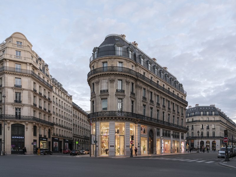 Curved masonry corner tower with mansard roof and illuminated ground floor retail space under cloudy sky